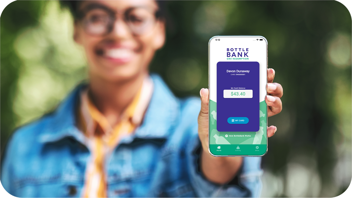 Young Black woman in a park smiling and holding up a smartphone displaying the BottleBank app.